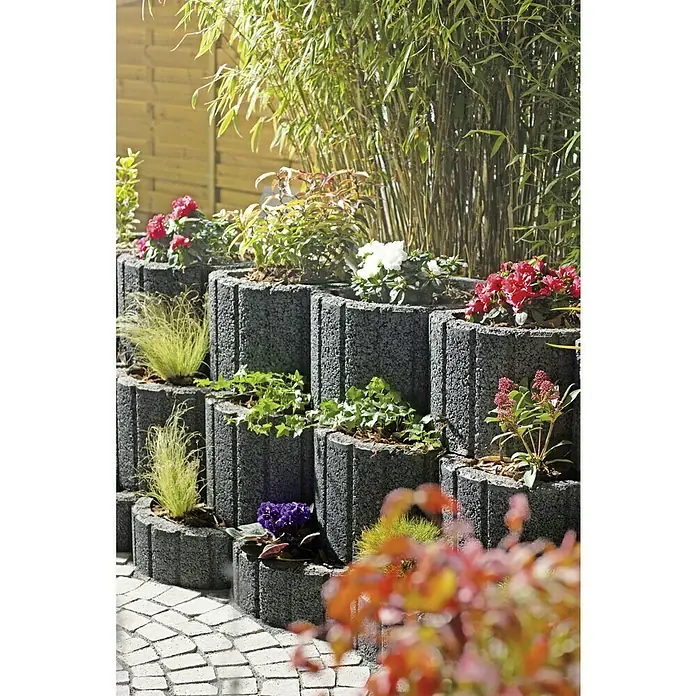 EHL Pflanzstein Stützflor - Anthrazit, 50 x 40 x 30 cm, Beton - Eine mehrstufige Mauer aus grauen Pflanzsteinen mit verschiedenen Pflanzen, die eine attraktive Gartengestaltung ermöglichen.