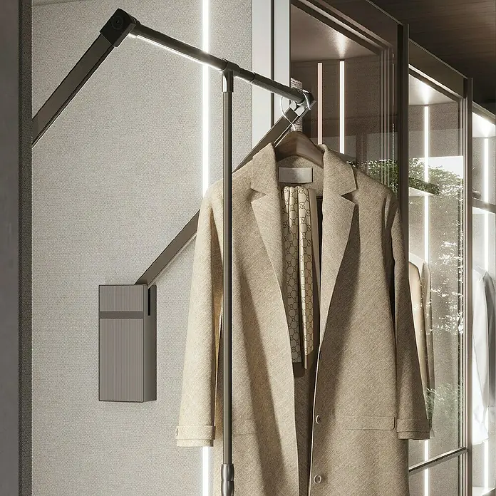 Emuca Kleiderstange Sway - Breitenverstellung: 830 mm - 1.150 mm, Titanium - Elegante Garderobe mit beigem Mantel und Schal, aufgehängt an einem ausziehbaren Kleiderlift vor beleuchteten Glasschränken.