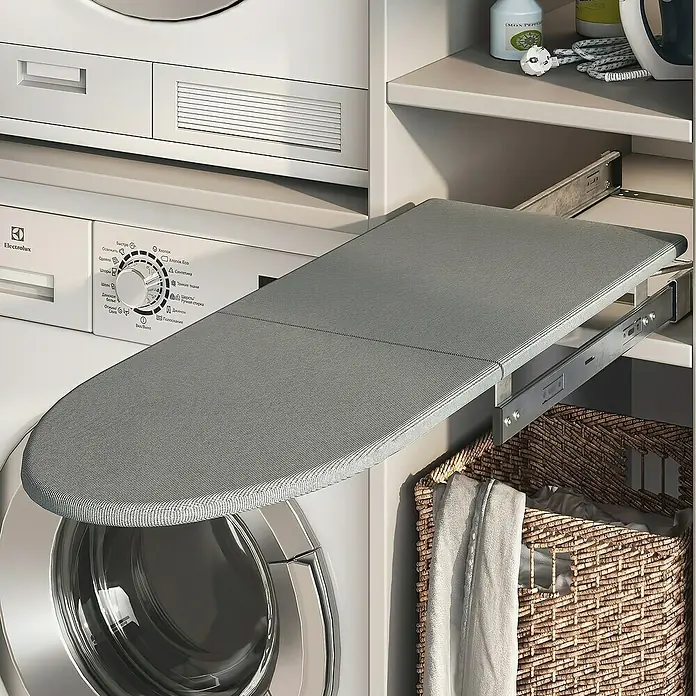 Emuca Bügeltisch Iron 2 Klapp- & ausziehbar - 89 x 30 cm - Graues Bügelbrett, das aus einem Schrank in der Nähe einer Waschmaschine herausgezogen wird, neben einem Wäschekorb.