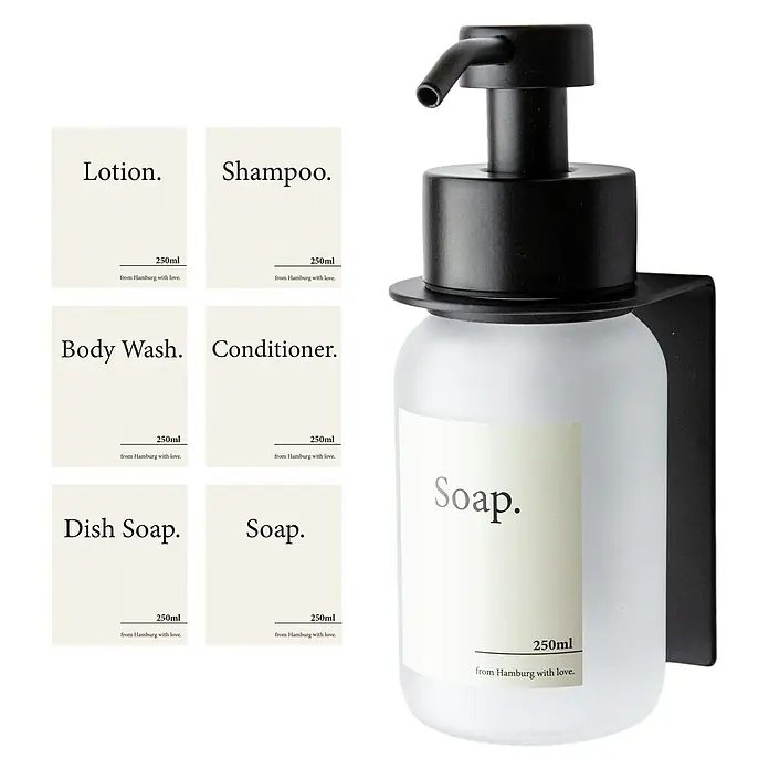 Designfabrik Hamburg Seifenspender - Edelstahl, Schwarz/Satiniertes Glas, Wandmontage - Bild eines Seifenspenders mit verschiedenen Etiketten, darunter Lotion, Shampoo, Spülmittel, Körperwäsche, Spülung und Seife.