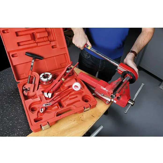 Rothenberger Industrial Werkzeugkoffer SANIKIT - 9 -tlg. - Eine rote Werkzeugkiste mit Rohrschneider, Rohrzange und weiterem Werkzeug neben einem Schraubstock mit einem Werkstück.