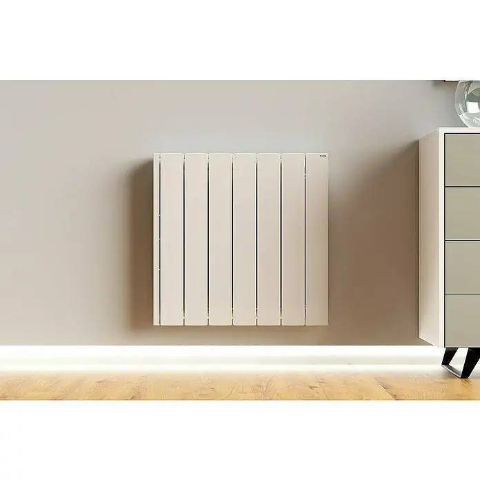 Rointe Emisor térmico Hera - 1.250 W, Blanco, 9 x 74 x 55 cm - Un radiador moderno de color crema cuelga en la pared, irradiando calidez y estilo. Complementa a la perfección el mueble moderno que hay al lado.