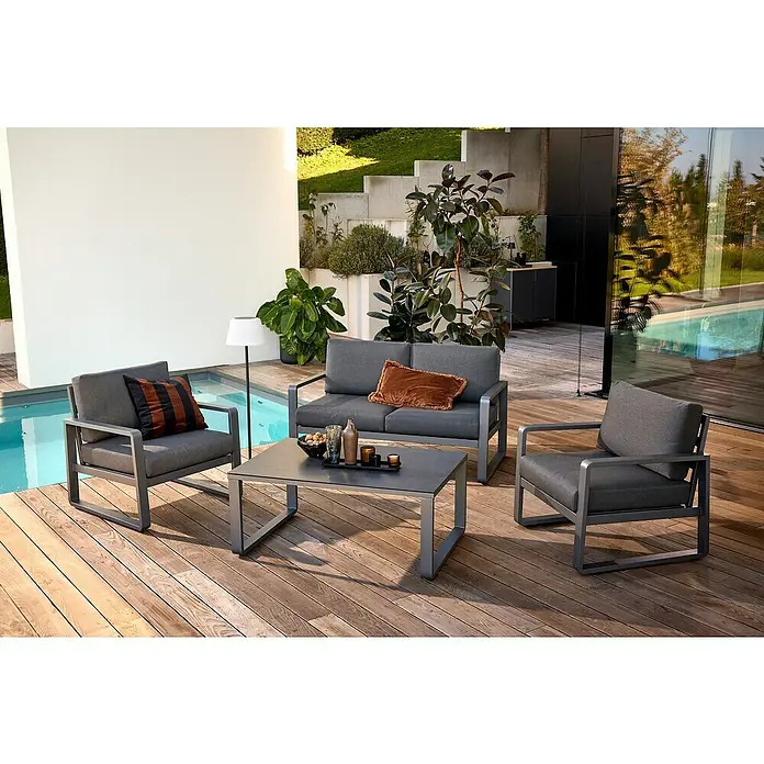 Sunfun Maja Loungemöbel-Set - 4 -tlg., Aluminium, Stahl, Sicherheitsglas, Olefin, Night-Grey - Eine moderne graue Gartenmöbelgruppe mit einem Sofa, zwei Sesseln und einem Tisch auf einer Holzterrasse neben einem Pool.