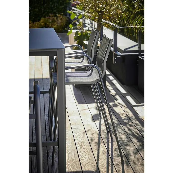 Sunfun Gastro Garten-Barhocker - Stahl, Textilen, Stapelbar, Night-Grey, B x T x H: 53,5 x 74 x 110 cm - Eine Nahaufnahme eines modernen Gartentisches mit Stühlen aus Metall und Netzstoff auf einer Holzterrasse im Freien.