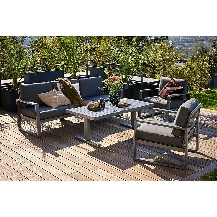 Sunfun Maja Loungemöbel-Set - 4 -tlg., Aluminium, Stahl, Olefin, Zwei Sessel, Tisch höhenverstellbar, Night-Grey - Graue Gartenmöbel-Lounge-Set mit Sofa, Sesseln und Tisch auf einer Holzterrasse, umgeben von Pflanzen und Stadtblick im Hintergrund.