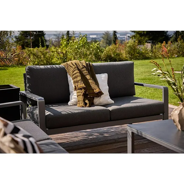 Sunfun Maja Loungesofa 2-Sitzer - B x T x H: 139,5 x 76 x 74,5 cm, Aluminium, Olefin, Night-Grey - Graue Gartenmöbel mit Kissen und Decke auf einer Holzterrasse, umgeben von Grün. Perfekt für entspannte Stunden im Freien.