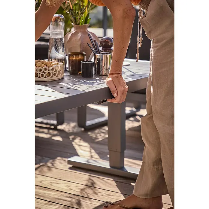 Sunfun Maja Garten-Loungetisch - L x B x H: 138,5 x 70 x 72 cm, Stahl, Night-Grey - Nahaufnahme eines modernen grauen Gartentisches mit stilvoller Dekoration und einer Person, die sich daran anlehnt.