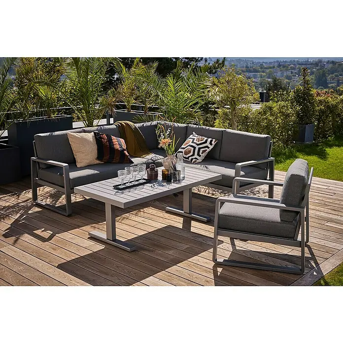 Sunfun Maja Loungesofa-Eckelement - Aluminium, Olefin, Night-Grey - Einladende Gartengarnitur mit grauem Sofa, Sessel und Tisch auf einer Holzterrasse, umgeben von üppigem Grün und einem Ausblick in die Ferne.