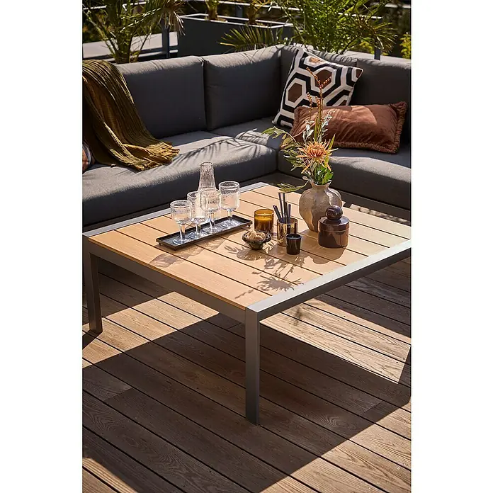 Sunfun Maja Loungetisch Holzoptik - L x B x H: 100 x 100 x 42 cm, Aluminium, Night-Grey - Ein quadratischer Couchtisch mit Holzplatte und grauem Rahmen steht auf einer Terrasse mit Lounge-Möbeln und Dekorationen.