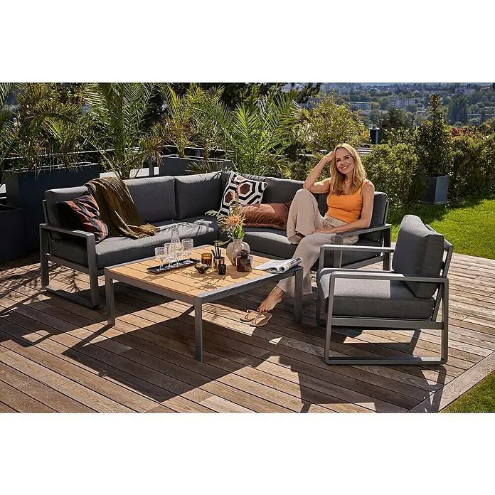 Sunfun Maja Loungesessel - B x T x H: 76 x 76 x 74,5 cm, Aluminium, Olefin, Night-Grey - Ein graues Lounge-Set im Freien mit einer Frau darauf. Das Set beinhaltet eine Couch, einen Sessel und einen Tisch mit Getränken.