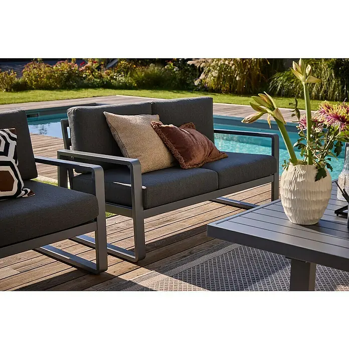 Sunfun Maja Loungesofa 2-Sitzer - B x T x H: 139,5 x 76 x 74,5 cm, Aluminium, Olefin, Night-Grey - Graues Gartensofa mit Kissen auf einer Holzterrasse neben einem Pool und einem Tisch mit Blumen. Stilvolle Outdoor-Möbel.