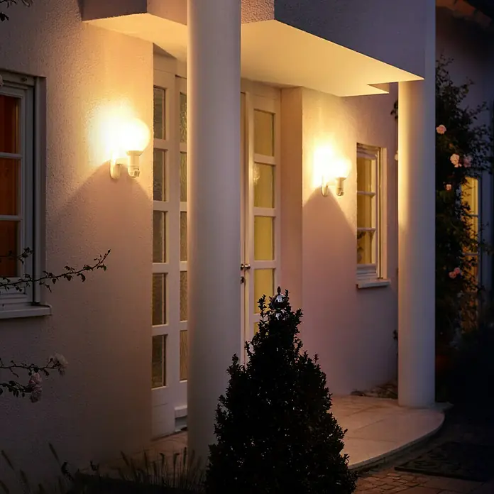 Steinel Sensor-Außenleuchte L 560 S schwarz - 60 W, 243 x 215 x 368 mm, Schwarz, IP44 - Außenaufnahme eines Hauses mit zwei beleuchteten Philips Hue Wandleuchten, die warmes Licht auf die Fassade werfen.