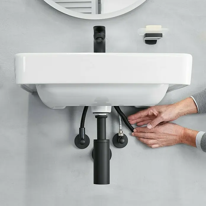 Schutzschlauch - Schwarz, Gesamtstückzahl: 2 Stk. - Detailaufnahme eines modernen weißen Waschbeckens mit schwarzen Armaturen und einem Siphon vor einer grauen Wand.