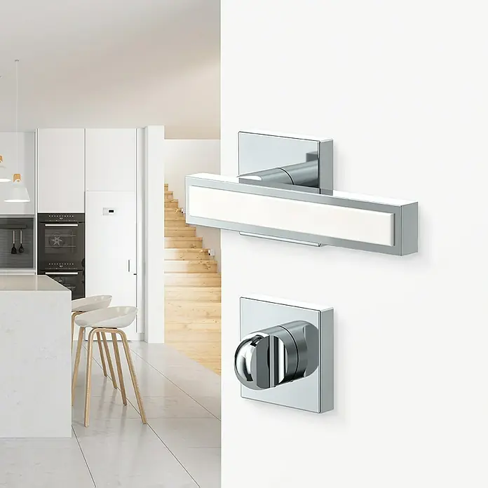 Diamond Doors Zimmertürgarnitur WC Tyler White - Chrom Weiß, Stärke Tür: 40 mm - 45 mm, Schlitzkopf/Olive - Wandmontierte Beleuchtung und Armatur mit verchromter Oberfläche vor einem modernen Küchenhintergrund.