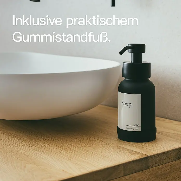 Designfabrik Hamburg Seifenspender - Edelstahl, Schwarz/Schwarz beschichtetes Glas - Eine schwarze Seifenflasche mit Aufdruck "Soap." und praktischem Gummifuß steht neben einem weißen Waschbecken auf einer Holzablage.