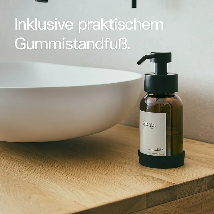 Designfabrik Hamburg Seifenspender - Edelstahl, Schwarz/Braunglas - Seifenspender aus braunem Glas mit schwarzer Pumpe und Gummifuß auf einem Holztisch neben einem Waschbecken.