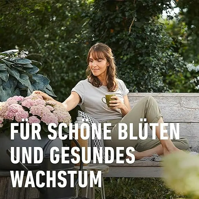 Compo Bio-Schafwolldünger Rhododendron & Hortensien - 2 kg, Hortensien - Frau sitzt auf einer Bank im Garten mit Blumen und Kaffee, während "Für schöne Blüten und gesundes Wachstum" angezeigt wird.
