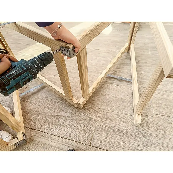 Astigarraga Holzklappbock Standard - Tragkraft: 400 kg, Höhe: 74 cm, Kiefer - Nahaufnahme einer Person, die ein Holzprodukt mit einem Akkuschrauber und einer Halterung zusammenbaut.