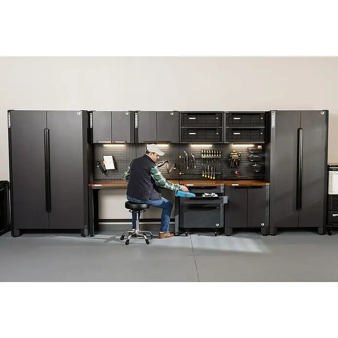 ToughBuilt Armario multiusos metálico - L x An x Al: 47 x 71 x 84 cm, Número de puertas: 2 ud. - Hombre sentado en un banco de trabajo Toughbuilt con cajones, encimera y almacenamiento de herramientas, ideal para garajes y talleres.