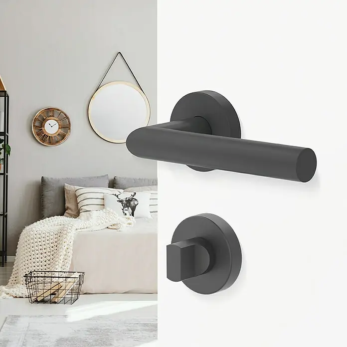 Diamond Doors Modern Zimmertürgarnitur WC L-Form - Stärke Tür: 40 mm - 45 mm, Schlitzkopf/Olive, Edelstahl, L-Form, Anthrazit - Ein modernes, anthrazitfarbenes Türgriff-Set, bestehend aus Drücker und Rosette, vor einem stilvollen Schlafzimmer-Hintergrund.