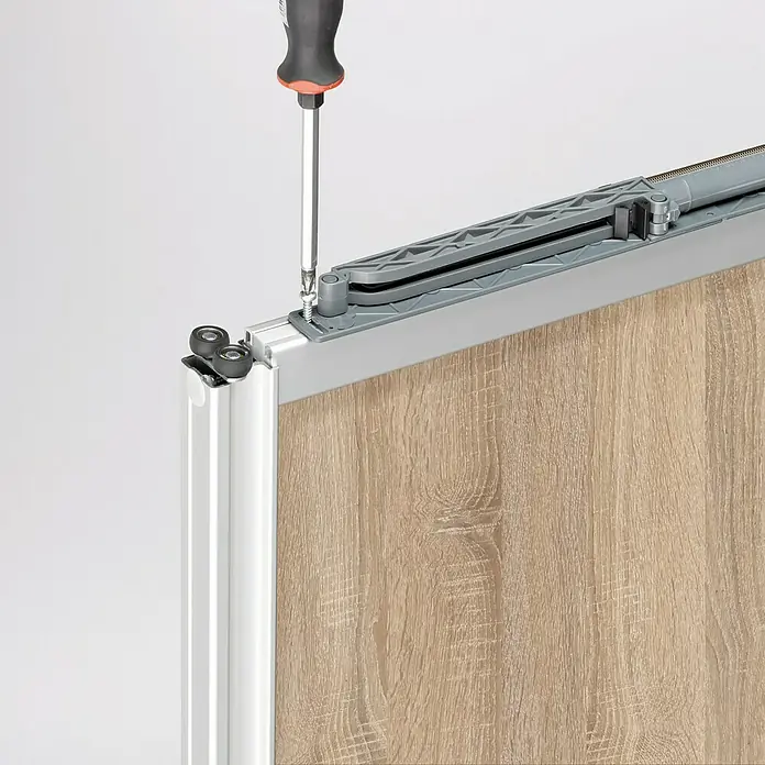 Room Plaza Easy Selbsteinzug für Schiebetüren - Passend für: Room Plaza Schiebetür-Bau-Sets - Detailaufnahme einer Schiebetür mit Schraubendreher, der eine Schraube befestigt. Fokus auf die Montage des Schiebetürsystems.
