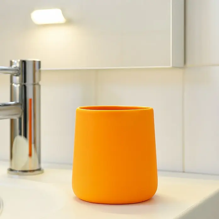 MSV Maonie Portacepillos - Ø x Al: 8,5 x 10 cm, Cerámica, Amarillo - Primer plano de un portacepillos de dientes naranja junto a un grifo moderno, destacando los accesorios de baño.