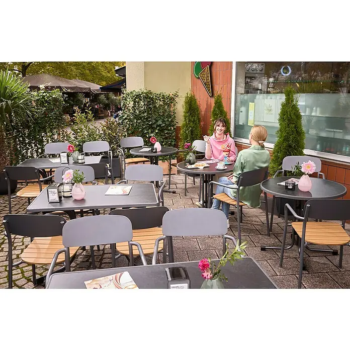 MFG Gartentisch Boulevard - L x B: 110 x 70 cm, Stahl, Mecalit, Schiefer, Klappbar - Außenbereich eines Cafés mit Tischen und Stühlen, an denen zwei Frauen sitzen. Ein Eiswaffel-Logo hängt an der Wand.