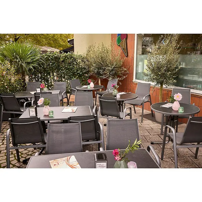 MFG Balkontisch rund Boulevard - Ø x H: 70 x 110 cm, Stahl, Mecalit, Klappbar, Anthrazit - Einladende Außenterrasse mit stilvollen grauen Tischen und Stühlen, dekoriert mit Blumenvasen, ideal für entspannte Stunden im Freien.