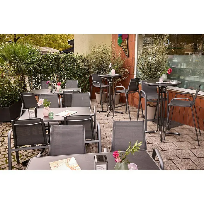 MFG Garten-Stehtisch rund - Ø x H: 70 x 110 cm, Stahl, Mecalit, Rund, Schiefer - Eine Außenaufnahme eines Cafés mit Tischen und Stühlen, dekoriert mit Blumen. Perfekt für eine entspannte Kaffeepause im Freien.