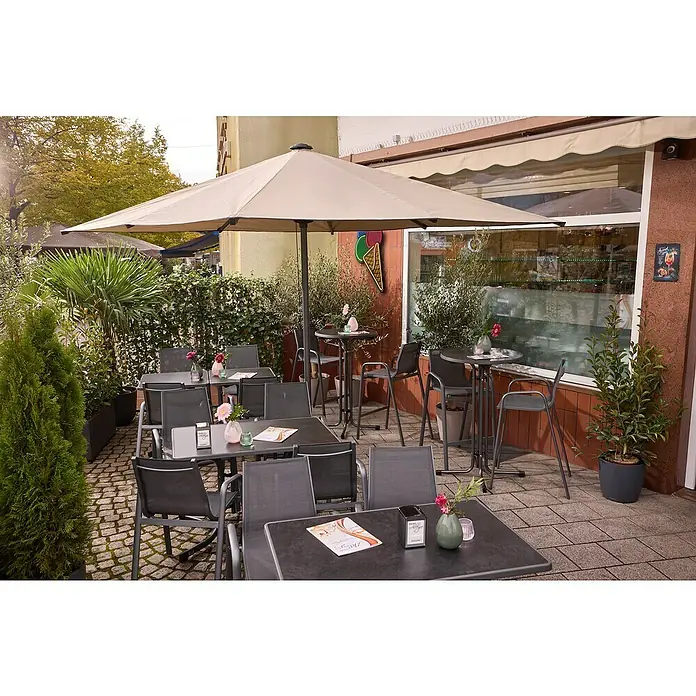 MFG Garten-Stehtisch rund - Ø x H: 70 x 110 cm, Stahl, Mecalit, Rund, Schiefer - Gemütlicher Außenbereich eines Cafés mit Tischen, Stühlen und einem großen Sonnenschirm, der Schatten spendet und zum Verweilen einlädt.