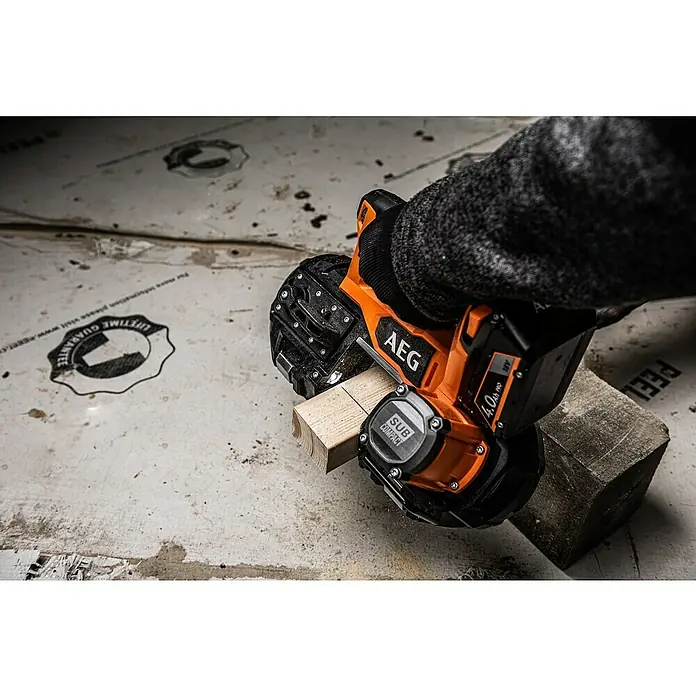 AEG Pro 18V Akku-Bandsäge BNS 18SBL-0 - 18 V, Ohne Akku - Nahaufnahme einer AEG-Säge, die ein Holzstück schneidet, mit Beton im Hintergrund, was ihre robuste Bauweise und Vielseitigkeit hervorhebt.