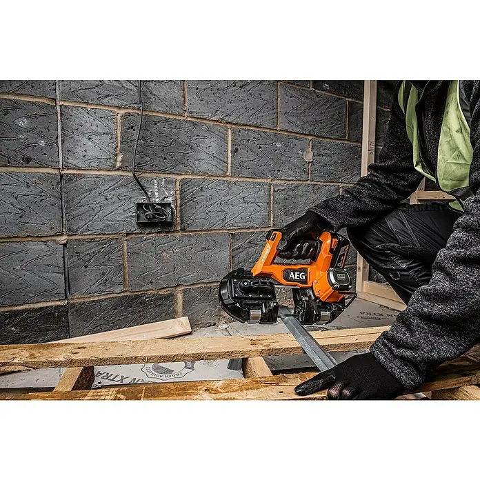 AEG Pro 18V Akku-Bandsäge BNS 18SBL-0 - 18 V, Ohne Akku - Nahaufnahme einer AEG Akku-Bandsäge beim Schneiden von Metall, bedient von einer Person in Arbeitskleidung vor einer Backsteinmauer.
