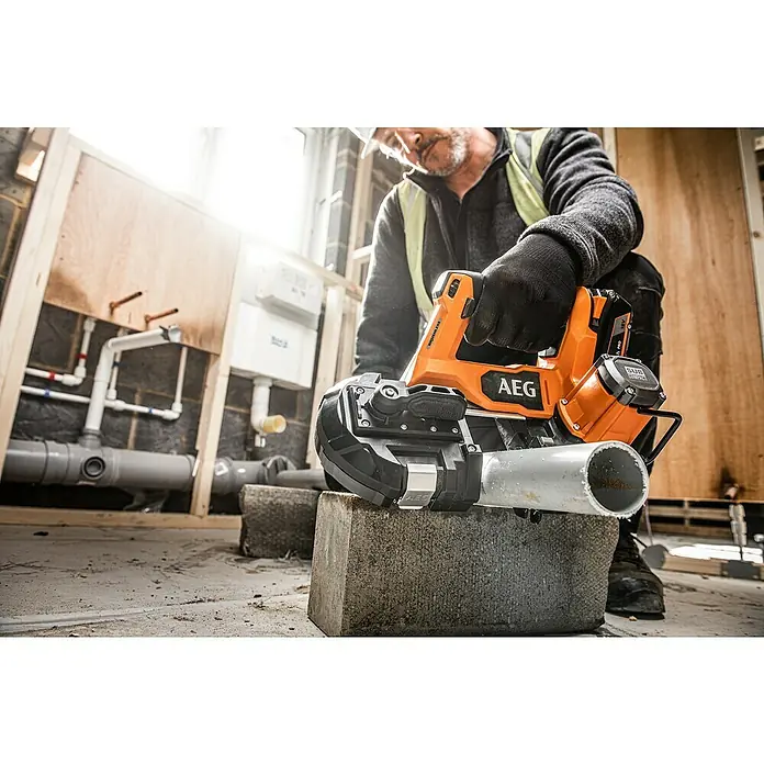 AEG Pro 18V Akku-Bandsäge BNS 18SBL-0 - 18 V, Ohne Akku - Ein Bauarbeiter benutzt eine AEG Akku-Bandsäge zum Zuschneiden eines Rohrs auf einer Baustelle. Die Säge ist orange und schwarz.
