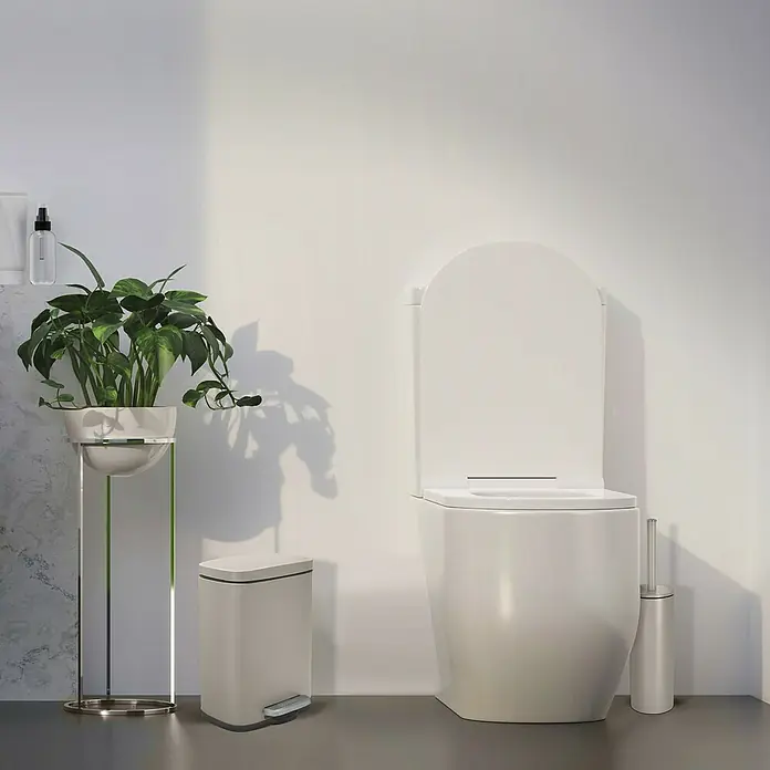 Spirella Cubo con pedal Akira - 5 l, Acero inoxidable, Topo - Un inodoro moderno con asiento elevado y forma redondeada, complementado con una papelera y una planta para un ambiente de baño elegante.
