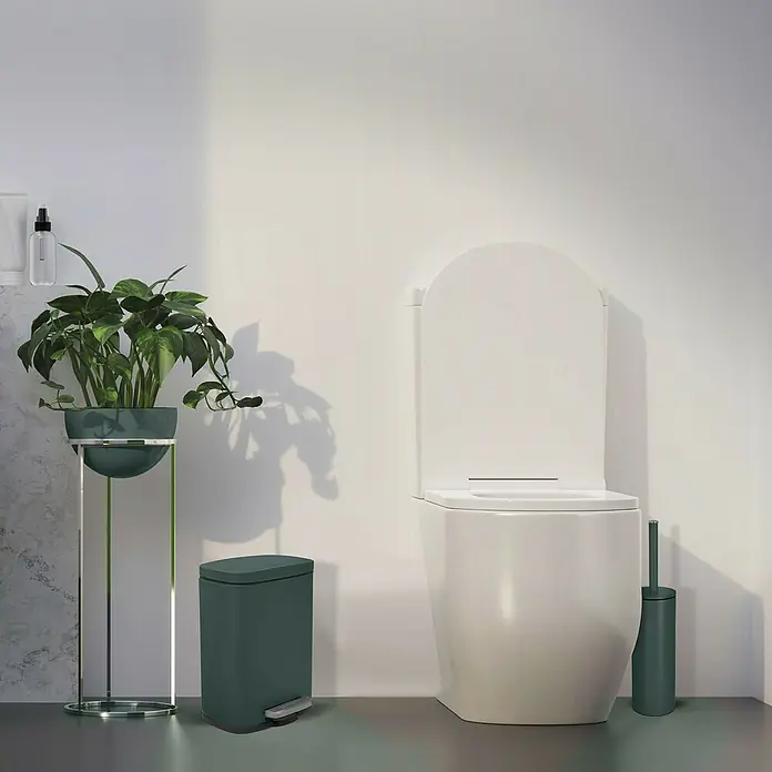 Spirella Cubo con pedal Akira - 5 l, Acero inoxidable, Verde oscuro - La imagen muestra un inodoro moderno con un cepillo a juego, un cubo de basura verde y una planta elegante en un soporte.