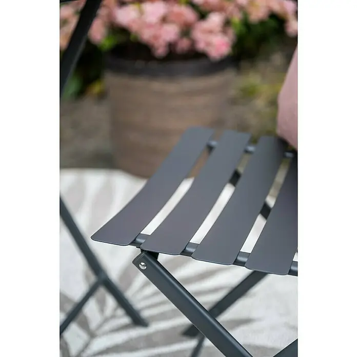 Garden Impressions Balkonmöbel-Set Alfa - 3 -tlg., Stahl, Schwarz - Nahaufnahme eines grauen Gartenstuhls mit Lamellensitz vor einem verschwommenen Hintergrund mit Blumen.