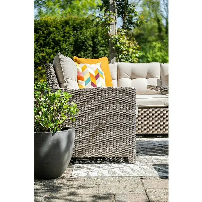 Garden Impressions Loungemöbel-Set Blue Bird - 4 -tlg., Aluminium, Polyester, Glas, Links, Beige - Nahaufnahme eines grauen Rattan-Sofas mit bunten Kissen und einem Topf mit grünen Pflanzen auf einer gepflasterten Terrasse im Freien.