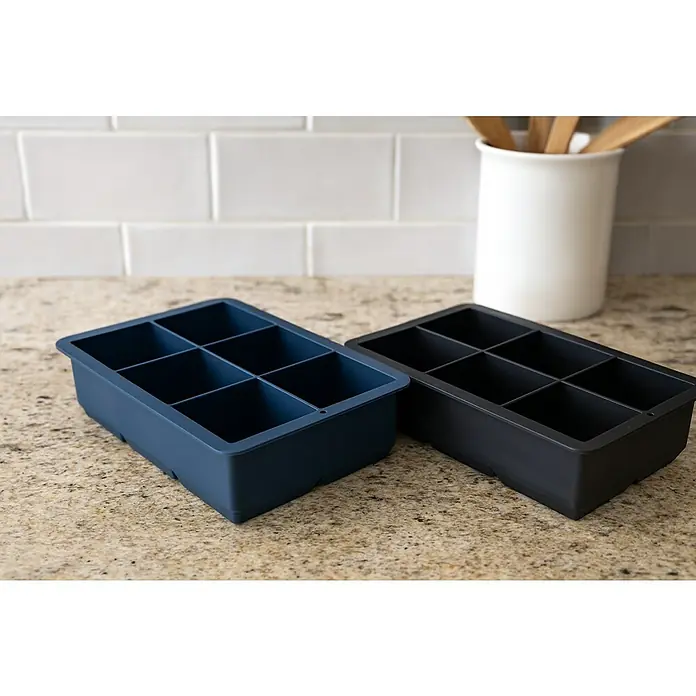Versa Cubitera - L x An x Al: 16 x 11,5 x 5 cm - Dos cubiteras de silicona, una azul y otra negra, sobre una encimera de cocina, ideales para cubitos de hielo grandes para bebidas.