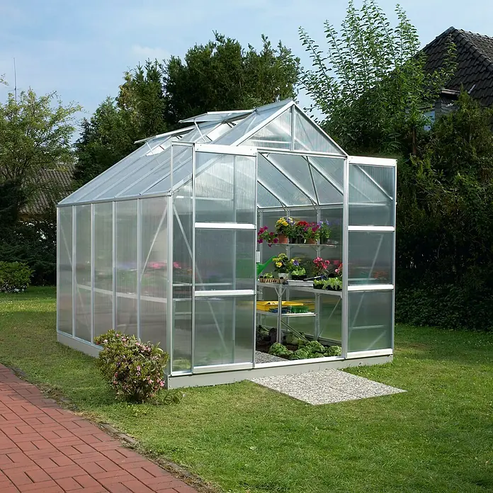 Vitavia Gewächshaus Mars 8300 Plus - Außenmaß inkl. Dachüberstand (B x T): 257 x 321 cm, 4 mm, Aluminium - Ein Gewächshaus aus Aluminium und durchsichtigem Kunststoff steht auf einer grünen Wiese. Im Inneren befinden sich Pflanzen auf Regalen.