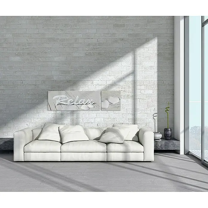 Glasbild - Relax III, B x H: 80 x 30 cm - Helles Wohnzimmer mit weißem Sofa und dekorativen Elementen an einer Ziegelwand. Das Tageslicht erhellt den Raum und betont die entspannte Atmosphäre.