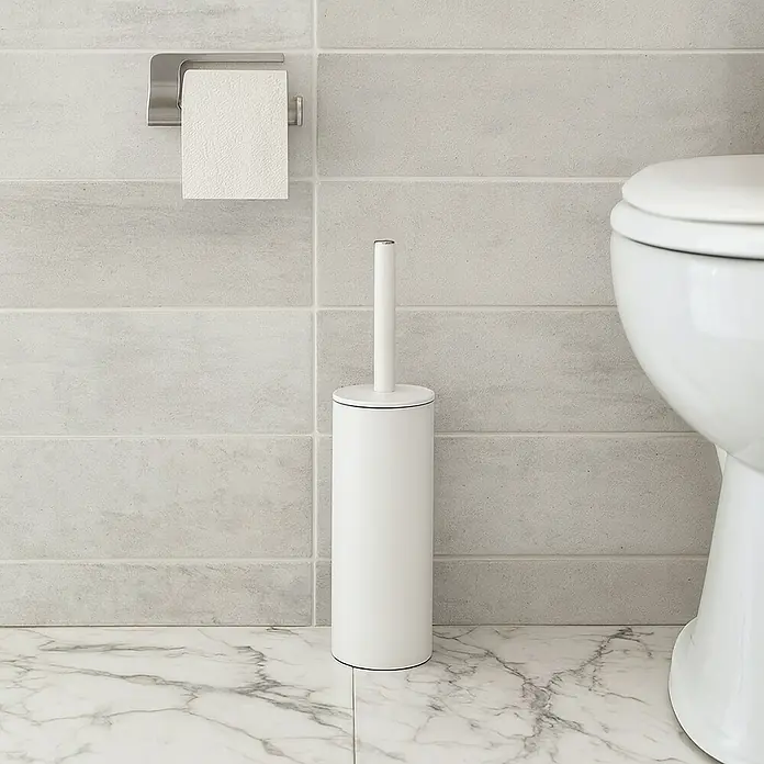 Spirella Conjunto de escobilla Akira - 9,5 x 9,5 x 40 cm, Acero inoxidable, Blanco - Vista de baño con un cepillo de inodoro blanco y un portarrollos contra una pared gris con suelo de mármol.
