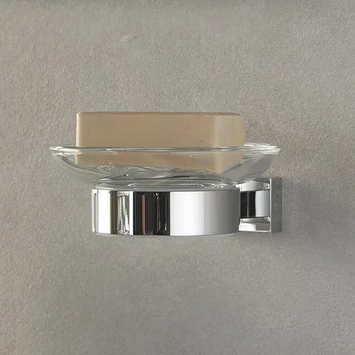 Grohe Essentials Cube Becher- & Seifenhalter - Chrom, Glänzend - Das Bild zeigt eine Wandseifenschale aus Chrom und Glas mit einem Stück Seife darauf, die an einer grauen Wand montiert ist.