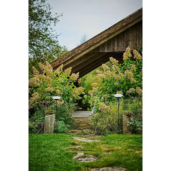 Lumix Solar-Dekoleuchte Sunny - Lichtfarbe: RGB, Höhe: 100 cm, Sunny - Gartenlandschaft mit Gartenleuchten, die den Weg zu einem überdachten Bereich beleuchten und eine gemütliche Atmosphäre schaffen.