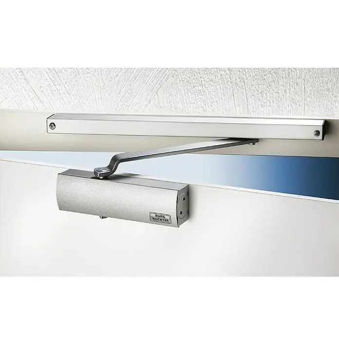 Burg-Wächter Türschließer GTS 513 - Silber, Geeignet für: Türen, Max. Türbreite: 95 cm - Türschließer von Burg Wächter an einer weißen Tür montiert, mit silbernem Gehäuse und Arm, der an einer Halterung an der Wand befestigt ist.