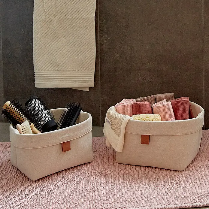 Store It Premium Bad-Aufbewahrungskorb - 22 x 18 x 16 cm, Baumwolle, Beige - Zwei Stoffkörbe, einer mit Bürsten, der andere mit Handtüchern, auf einem rosa Teppich.