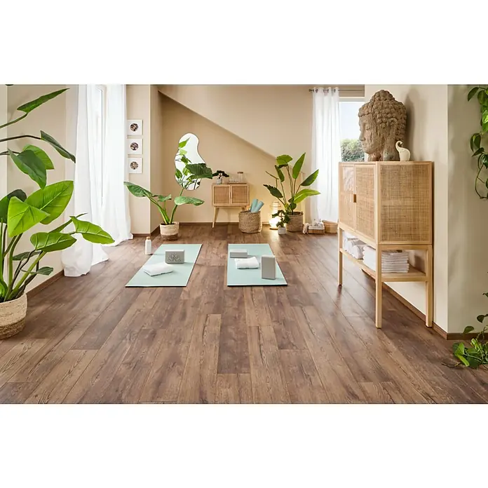 LOGOCLIC Ambienta Laminat - Eiche Mirandola, Landhausdiele, 1.288 x 195 x 10 mm - Einladender Raum mit Holzboden, Yogamatten und einer Kommode mit Buddha-Statue für eine entspannende Atmosphäre.