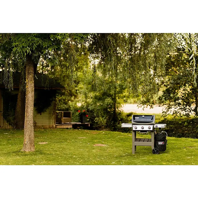 Weber Barbacoa de gas Spirit II E-310 + 7 accesorios - Superficie de la parrilla (An x Pr): 60 x 46 cm, 8,7 kW, Número de quemadores: 3 - Una barbacoa de gas Weber se encuentra en un exuberante césped verde, lista para una relajante parrillada al aire libre.