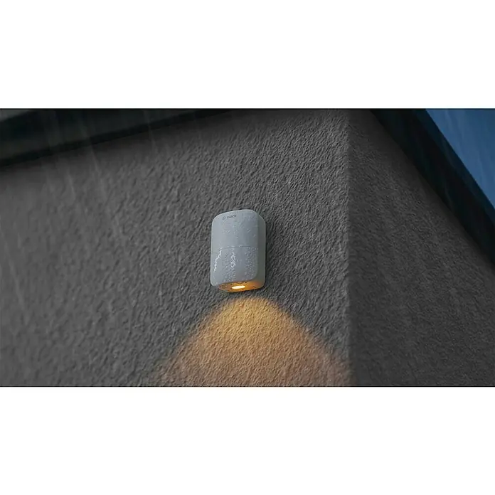 Bosch Smart Home Bewegungsmelder II [+M] Matter - weiß - Weiße BOSCH Außenleuchte an einer grauen Wand. Die Lampe scheint und ist mit kleinen Wassertropfen bedeckt.