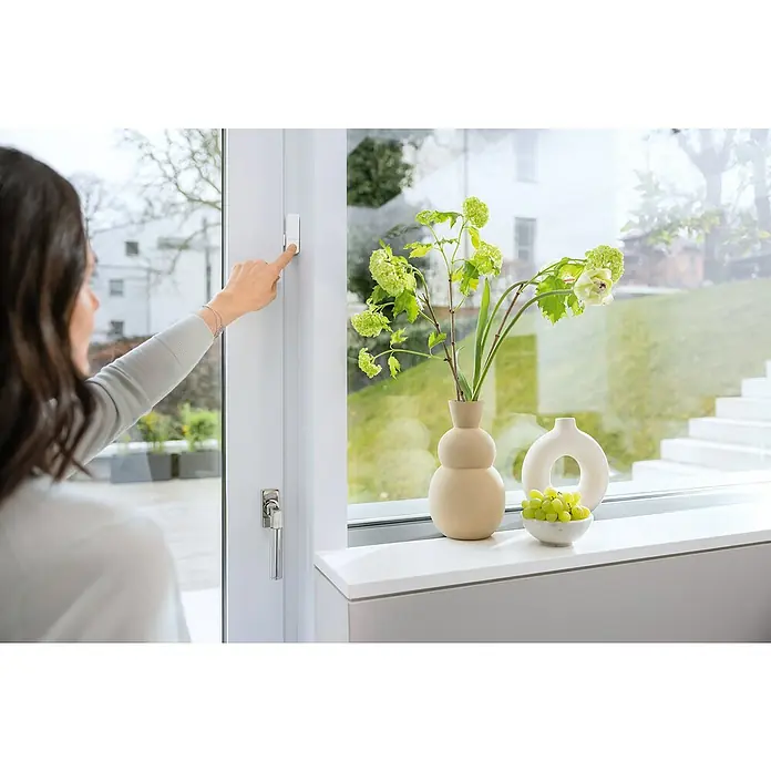 Bosch Smart Home Funk-Fensterkontakt II [+M] Matter - Weiß, Batteriebetrieben, 23 x 22 x 75 mm, 3 Stk. - Eine Frau bedient einen smarten Fensterkontakt, der für Sicherheit sorgt. Der Fensterkontakt ist unauffällig und leicht zu bedienen, er erhöht den Wohnkomfort.