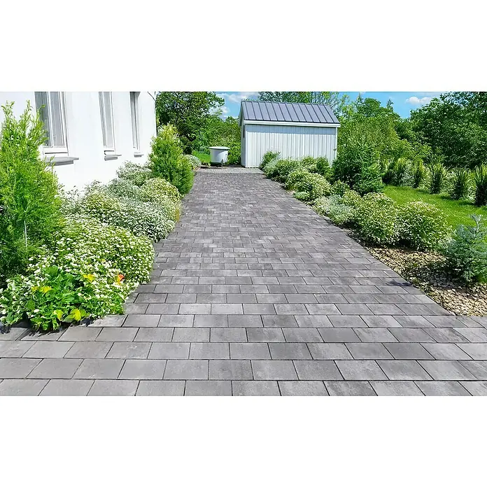 EHL EIBA Pflasterstein - 33 x 16,5 x 8 cm, Grau-Anthrazit, Beton - Eine gepflasterte Auffahrt führt durch einen üppigen Garten zu einem hellen Schuppen, der einen einladenden Zugang zum Haus bietet.